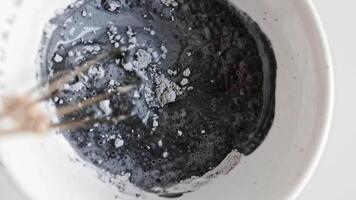 mezcla un carbón cara máscara con macro partículas un muestra de un cosmético fregar para limpieza el piel. parte superior ver de negro arcilla y barro cara mascarilla. spa relajación y disfrute video