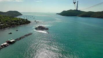 Aerial view of a luxury yacht and speedboat cruising in turquoise waters near a tropical island with a cable car system in the background Phu Quok video