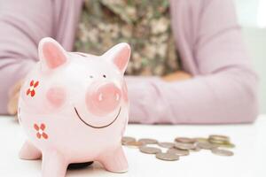 Retired elderly woman counting coins money with piggy bank and worry about monthly expenses and treatment fee payment photo