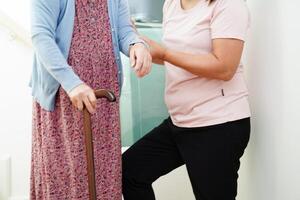 Asian senior woman use walking stick with caregiver help support walking down the stairs prevent accident, slip and fall at home. photo