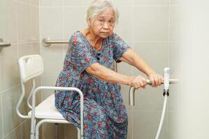 Asian elderly old woman patient use toilet support rail in bathroom, handrail safety grab bar, security in nursing hospital. photo