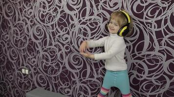 Little happy child dancing on sofa and listening music in headphones at home video