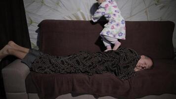 pequeno menina dentro roupão de banho acordando dela pai acima. homem dorme em a sofá video