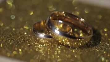 Wedding gols rings lying on shiny glossy surface. Shining with light. Close-up video