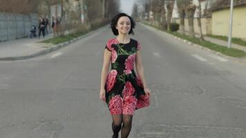 atraente jovem mulher dentro uma vestir com flores caminhando em a rodovia video