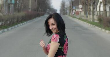 Attractive young woman in a dress with flowers turns to camera and smiles video