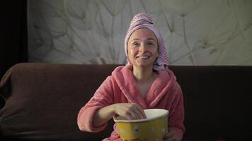 Woman watching a late night movie at TV, eating popcorn. Bathrobe, facial mask video