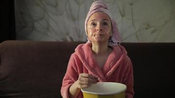 mujer acecho un tarde noche película a televisor, comiendo Palomitas. bata de baño, facial máscara video