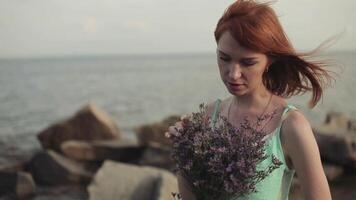 lent mouvement. magnifique sexy fille avec longue rouge cheveux dans une turquoise robe détient une bouquet de fleurs dans sa mains video