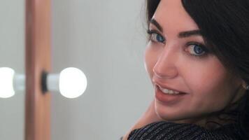 close-up. attractive young girl with blue eyes posing and smiling while looking at the camera in a beauty salon in front of a mirror with light bulbs. slow motion video