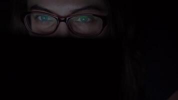 fille dans des lunettes fait du un en ligne achat en utilisant une mobile ordinateur mensonge sur une lit à Accueil à nuit. isolé lumière 4k video
