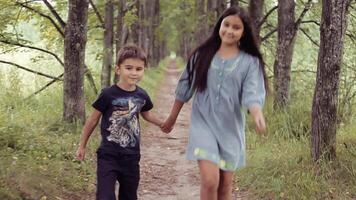 A beautiful little girl with long hair in a dress and a little boy running through the forest holding hands and smiling. The boy is pointing at something interesting video