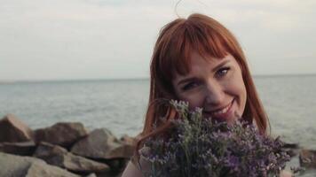 Portrait. Close-up. Slow motion. A beautiful young sexy model with long red hair in a long dress with a beautiful face has a romantic mood and holds flowers in her hands. video