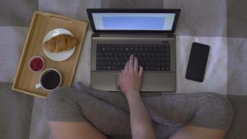 Overhead shot, creative girl working on a laptop sitting on a bed in stockings, looking at a revenue chart on a mobile phone. Homework. 4K video