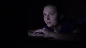 A woman works using a mobile computer while lying on the bed at home at night. Isolated light 4K video