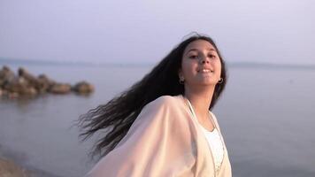 une magnifique fille avec longue cheveux dans une plage tunique se tourne autour se et sourit ayant une bien ambiance. lent mouvement. video