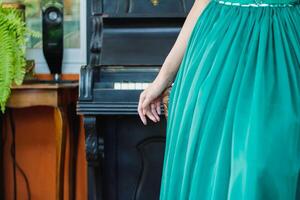 A woman in a long green dress leaned beside an ancient piano waiting for a piano practice before performing on stage at night. photo
