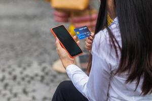 joven mujer es compras en línea mediante móvil solicitud por pago con su crédito tarjeta conveniencia de pago mediante compras en línea. concepto de en línea compras y gasto mediante crédito tarjeta. foto