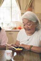 Portrait of an elderly Japanese woman with gray hair eating rice with chopsticks. photo