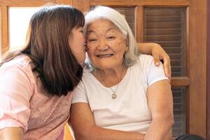 Affectionate Asian daughter kissing her mother at home. Mother's Day. photo