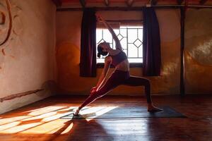 joven Delgado mujer haciendo yoga en pie en estera adentro. iluminar desde el fondo. foto