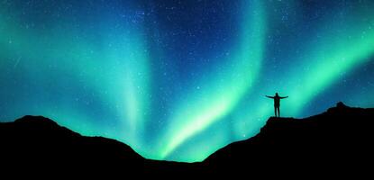 alpinista en pie en parte superior de montaña con Aurora borealis brillante en el noche cielo en ártico circulo foto