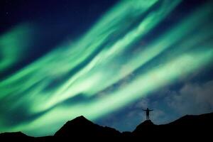 alpinista en pie en parte superior de montaña con Aurora borealis brillante en el noche cielo en ártico circulo foto