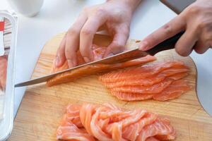 Hand cook using knife slicing a fresh salmon on chopping block photo
