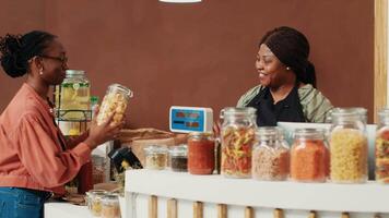 Customer shopping for pasta and organic bio sauces in jars, bringing various products to checkout counter. African american client discussing with vendor about sustainable lifestyle. video