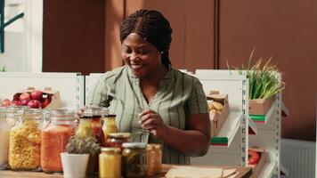 Woman client filling in paper bag with pasta sold as bulk item, buying various types of organic additives free products from local farmers market. Buyer searching for bio pantry supplies. video