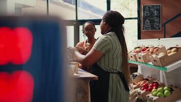 afrikansk amerikan Säljare ger mat prov till shoppare, rekommenderar hemlagad snacks med organisk Ingredienser. vegan klient påfrestande ut matvaror Lagra Produkter innan uppköp. handhållen skott. video