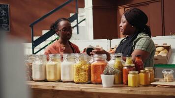 africain américain vendeur donnant nourriture échantillon à client, en présentant Nouveau fait maison collations avec Naturel ingrédients. végétalien femme en essayant en dehors marché des produits avant achat. ordinateur de poche tir. video