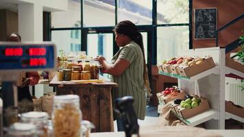 africano americano cliente torrencial varios abultar productos desde frascos, comprando orgánico hecho en casa mercancías almacenado en reutilizable contenedores vegano mujer elegir bio artículos a mercado. Mano disparo. video