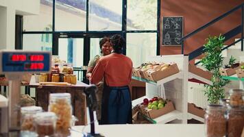 employé apportant la fourniture de fraîchement récolté produire à local supermarché, parlant à vendeur à propos durable mode de vie. fournisseur en portant caisses de marchandises, femme recevoir des produits. ordinateur de poche tir. video