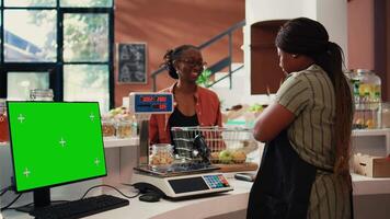 Shopper purchasing goods next to greenscreen on monitor, isolated mockup template on pc at cash register in supermarket. Vendor working with display running copyspace layout. Tripod shot. video