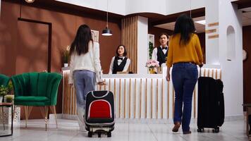 Asian guests approach reception to ask about accommodation, arriving at hotel and hoping for an early check in. Front desk staff team welcoming women and offering their services. Tripod shot. video