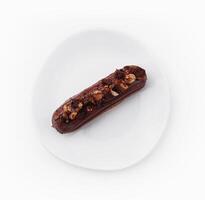 eclair with chocolate and nuts on a white plate photo