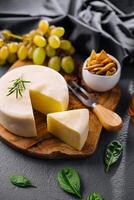 Round cheese on a wooden board and green grapes photo