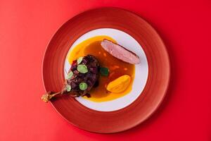 duck leg with pumpkin puree on red plate photo