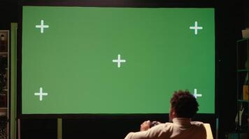 uomo seduta su divano a casa, rilassante di giocando videogiochi su isolato schermo ultrawide inteligente tv. gamer svolgimento nel appartamento di competere nel in linea multiplayer gioco visualizzato su croma chiave dispositivo video