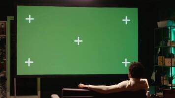 African american man watching football competition live on widescreen chroma key smart TV, cheering for favorite team. Sports fan on couch in front of green screen television set celebrating goal video