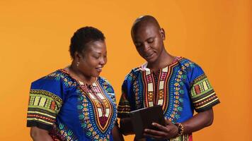 Ethnic couple navigating on social media app using tablet, looking at pictures and reading messages in studio. Young man and woman having fun scrolling website pages, online network. video