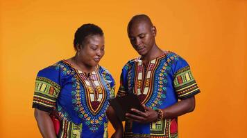 Ethnic people navigating on social media webpage, checking messages and looking at photos over orange background. African american man and woman scrolling online websites in studio. video