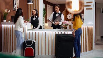 Hotel employees greeting customers at front desk in lobby, preparing for check in process. Receptionist looking for room reservation details, travelers confirming booking accommodation. video