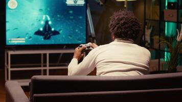 Gamer playing classic arcade space shooter videogame on big smart TV, shooting asteroids using laser beams. Man relaxing at home using high tech gaming console to solve missions in singleplayer game video