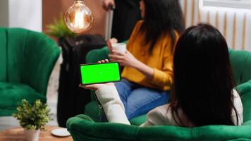 Asian traveler using smartphone with blank greenscreen at hotel, looking at template with chromakey and isolated mockup on display. Woman using phone and relaxing in lounge area. video