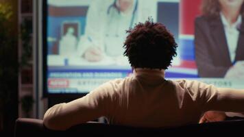 Man watching medical AI news discussed by presenter, displayed on smart TV in neon lit apartment. Person following newscast about artificial intelligence on video on demand channel, close up shot