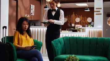 Waiter serving cup of coffee for customer in lounge area, waiting to be called at reception for room confirmation. Tourist arriving at hotel and relaxing with drink before check in, holiday trip. video