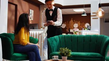 Hotel guest paying for coffee order at pos terminal, buying drink to relax after travelling by plane. Asian woman sitting in lounge area waiting for registration, making electronic payment. video