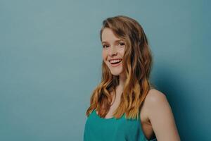 Radiant young woman with wavy hair and green top laughing joyfully against a cool blue background photo